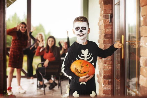 Ragazzo e bambini in costume e trucco festivo con lanterna di zucca Jack che bussa alla porta per dolci ad una festa di Halloween sulla strada vicino alla casa — Foto Stock