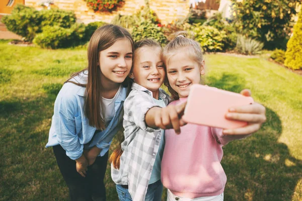 Skupina šťastných dospívajících dívek se směje a bere selfie na mobilní telefon venku. — Stock fotografie