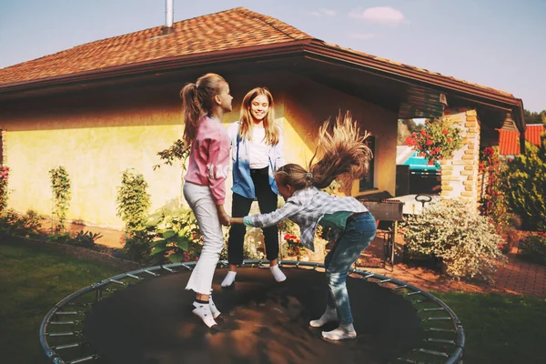 Feliz tres niños están saltando en un trampolín en el jardín cerca de su casa. —  Fotos de Stock