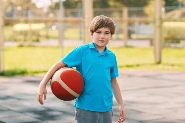 Potret seorang anak laki-laki tersenyum dalam seragam olahraga dengan bola basket di tangannya. Seorang anak laki-laki memegang bola di tangannya setelah bermain basket. — Stok Foto