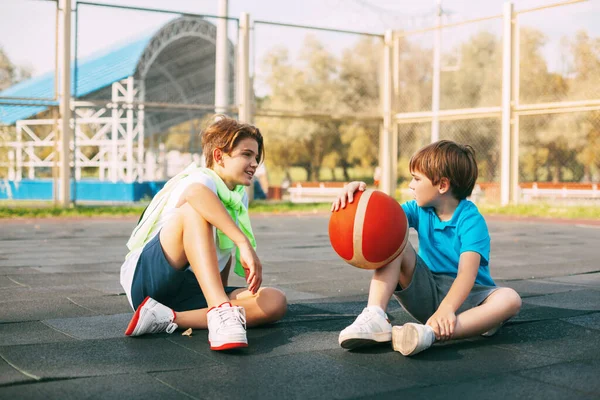 Remaja laki-laki duduk di lapangan basket dan bersantai setelah latihan. — Stok Foto