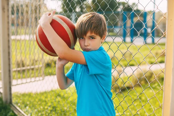 Potret seorang anak laki-laki yang indah dalam seragam olahraga dengan bola basket di tangannya. — Stok Foto