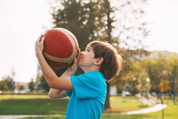 파란 운동복을 입은 귀여운 소년이 농구공을 바구니에 던져 넣을 준비를 하고 있는 모습. 아이가 농구를 한다. — 스톡 사진