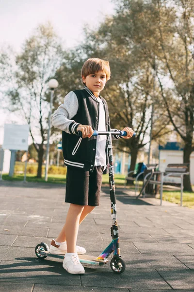 Güzel bir çocuk parkta scooter sürüyor. Çocuk temiz havada aktif bir zaman geçirir. Sağlıklı yaşam tarzı ve spor eğlencesi