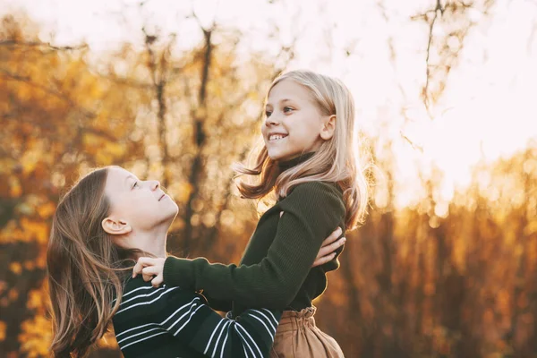 Duas irmãs meninas felizes rindo, se divertindo e brincando na queda na natureza ao ar livre no parque de outono — Fotografia de Stock