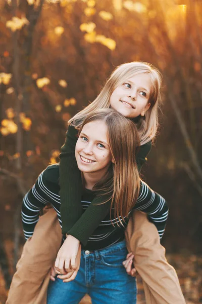 Twee gelukkige meisjes zussen lachen, plezier hebben en spelen in de herfst in de natuur buiten in het herfstpark — Stockfoto