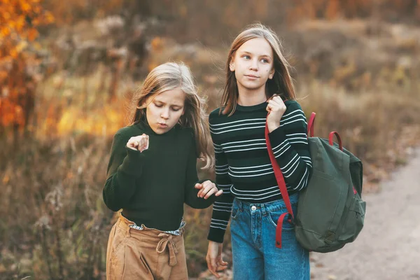 Las dos hermanas regresan de la escuela y hablan mientras conducen a través de un parque de otoño al aire libre. — Foto de Stock
