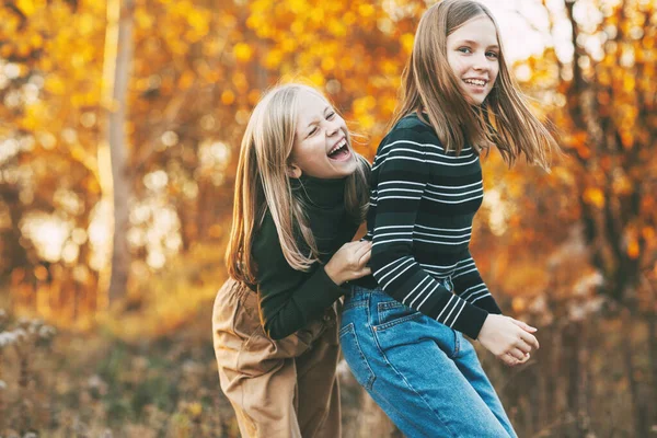 Dos hermanas niñas felices riendo, divirtiéndose y jugando en el otoño en la naturaleza al aire libre en el parque de otoño —  Fotos de Stock