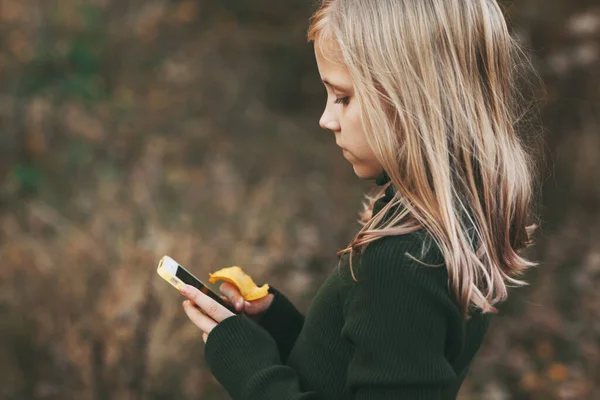 Rubia adolescente se para con el teléfono y escribe un mensaje en el parque al aire libre. —  Fotos de Stock