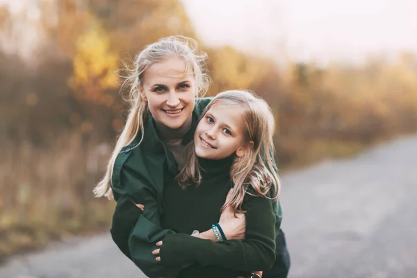 Portret van gelukkig volwassen moeder en haar blonde dochtertje knuffelen en lachen tijdens het wandelen in de herfst park buiten. — Stockfoto