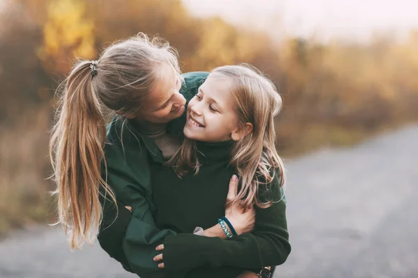 Portret van gelukkig volwassen moeder en haar blonde dochtertje knuffelen en lachen tijdens het wandelen in de herfst park buiten. — Stockfoto