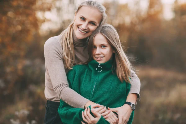 Portret van gelukkig volwassen moeder en haar blonde dochtertje knuffelen en lachen tijdens het wandelen in de herfst park buiten. — Stockfoto