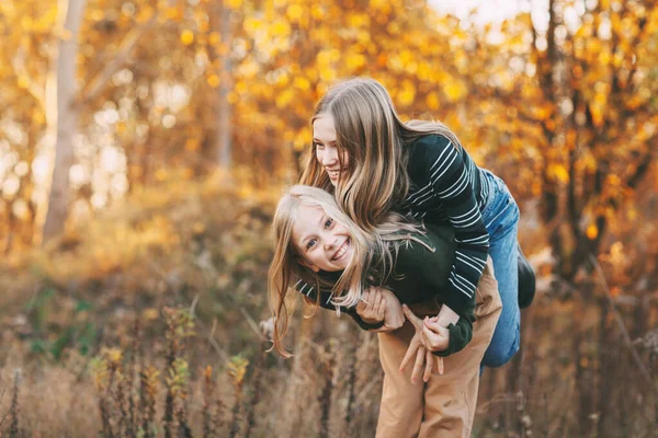 Duas irmãs meninas felizes rindo, se divertindo e brincando na queda na natureza ao ar livre no parque de outono — Fotografia de Stock