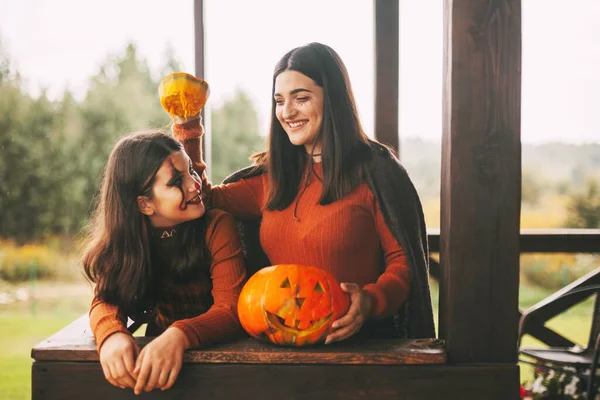 Due sorelle festeggiano Halloween per strada vicino alla casa in costume e trucco con una lanterna di zucca, giocano e ridono — Foto Stock