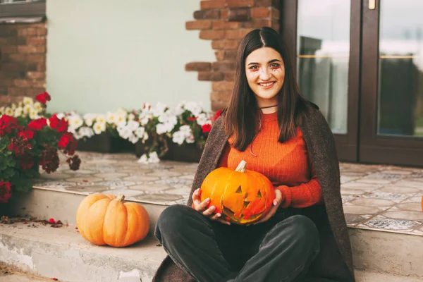 Una bella ragazza con i capelli scuri con il trucco per la celebrazione di Halloween tiene una zucca tra le mani e sorride. — Foto Stock
