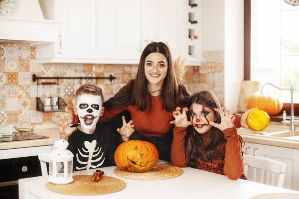 I bambini felici festeggiano Halloween in cucina a casa in costume e trucco con la lanterna di zucca Jack guardando la fotocamera e sorridendo — Foto Stock