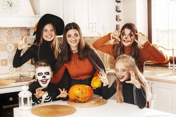 Happy kids celebrate halloween in kitchen at home in costumes and make-up with pumpkin lantern Jack looking at camera and smiling — Stock Photo, Image