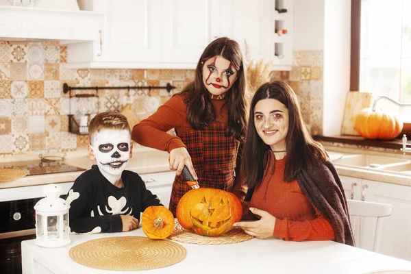 I bambini felici festeggiano Halloween in cucina a casa in costume e trucco con la lanterna di zucca Jack guardando la fotocamera e sorridendo — Foto Stock
