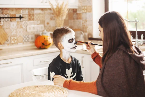 Az idősebb nővér befesti a bátyját otthon a konyhában Halloweenkor. Felkészülés Halloweenre. — Stock Fotó