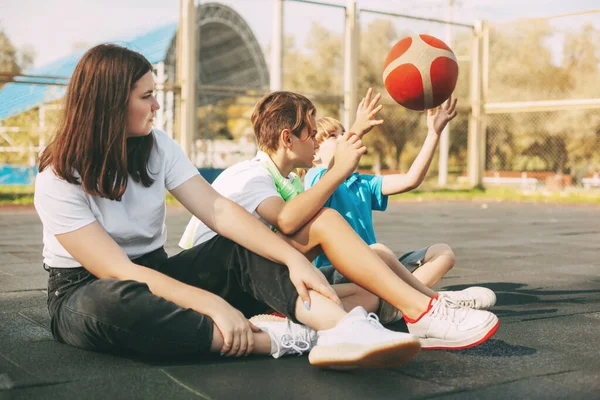 쾌활 한 고등학생들이 농구 코트에 앉아 경기가 끝난 후 긴장을 풀고 이야기하고 웃는다. 스포츠, 게임, 교육. 우정이라는 개념 — 스톡 사진