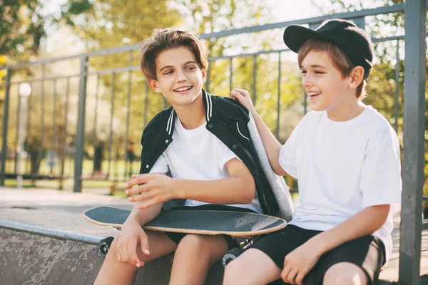 Dua remaja lucu duduk di skatepark, bersantai setelah skateboard dan chatting. Anak laki-laki menikmati waktu luang mereka di skate Park, duduk di jalan. Konsep pemuda, persatuan dan persahabatan — Stok Foto