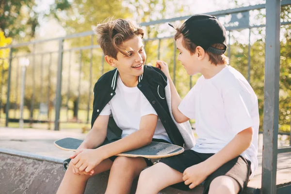Zwei niedliche Teenager sitzen in einem Skatepark, entspannen sich nach dem Skateboarden und unterhalten sich. Jungen genießen ihre Freizeit im Skatepark, sitzen auf der Rampe. Das Konzept von Jugend, Einheit und Freundschaft — Stockfoto
