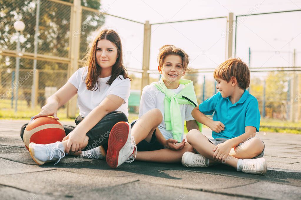Portrait of teenagers sitting on a basketball court. Children relax after the game, talk and laugh. Sports, games, and education. The concept of friendship