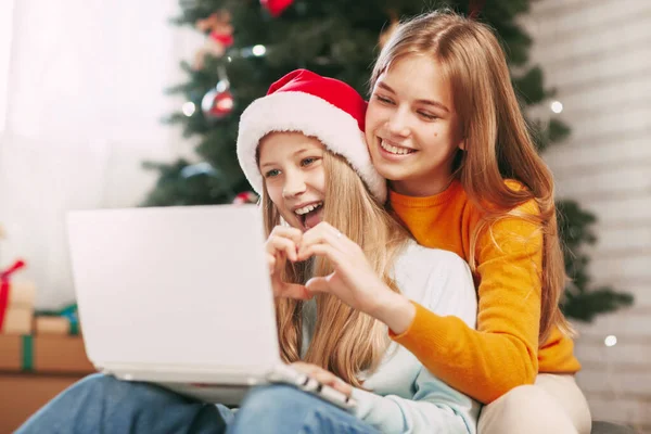 Two happy teenage sisters with blonde European looks communicate via laptop via video link with friends and grandparents on Christmas Day. Social distancing on New Years Eve.