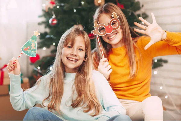 Due sorelline bionde dall'aspetto europeo guardano la cornice e sventolano la mano, comunicando tramite un tablet mobile tramite collegamento video con amici e nonni per Natale.. — Foto Stock