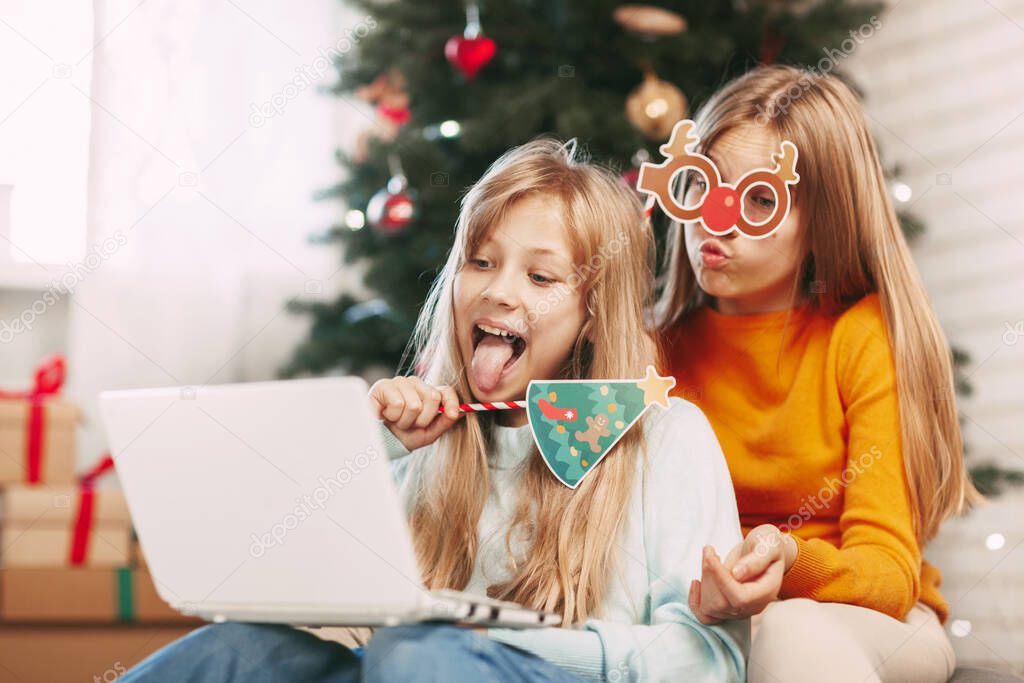 Two happy teenage sisters with blonde European looks communicate via laptop via video link with friends and grandparents on Christmas Day. Social distancing on New Years Eve.