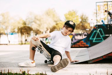 Bir çocuk parkın özel bir bölgesinde kaykay üzerinde numaralar yapıyor. Bir çocuk kaykay parkında kayarken düştü. Çocuk eğleniyor. Temiz havada aktif dinlenme