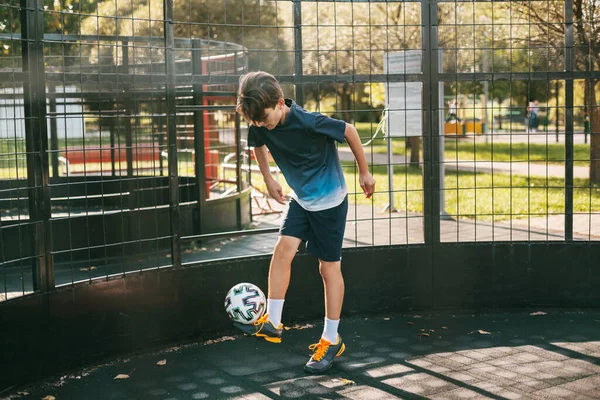 Spor üniformalı genç bir adam serbest stil futbol sahasında topla antrenman yapıyor. Bir futbolcu topla oynar. Spor, eğlence, eğitim, serbest stil