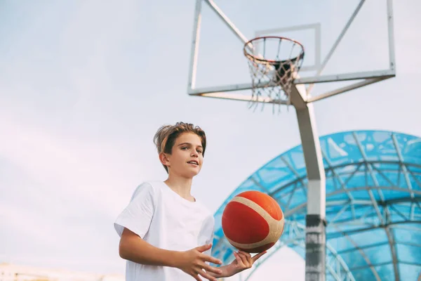 Seorang pemain basket berdiri di lapangan basket dan melempar bola basket ke tangannya. Konsep olahraga dan gaya hidup sehat — Stok Foto