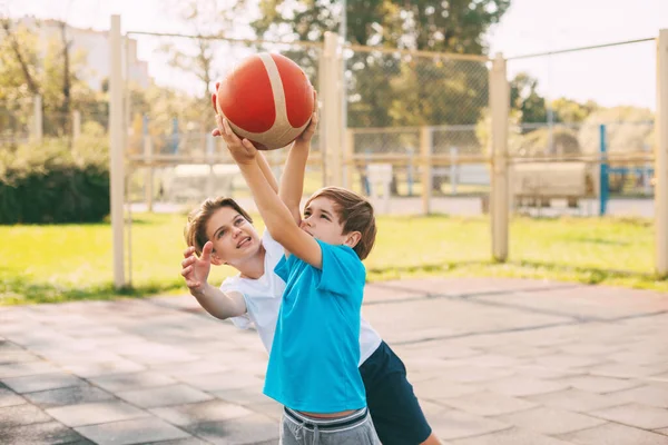 İki genç çocuk oyun sahasında basketbol oynuyor. Sporcular maçta top için savaşırlar. Sağlıklı yaşam tarzı, spor, motivasyon