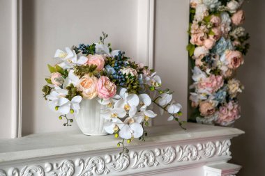 Peonies, orkide ve yaban mersini bir klasik tarzda beyaz bir şömine üzerinde beyaz bir saksı içinde bir buket