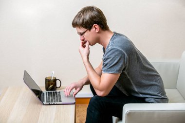 Genç adam gözlüklü bir ev ofis içinde bir laptop üzerinde yoğunlaşmıştır. İkindilerde ekrandaki metinleri tarar. yan görünümü. yatay çekim