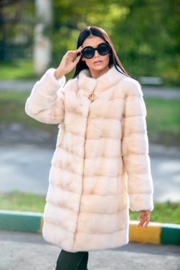 Güneş gözlüğü ve hafif bir kürk güzel esmer sokakta yürüyor ve uzak görünüyor