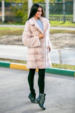 Güzel esmer bir açık renkli kürk ceket ve siyah pantolon aşağı belgili tanımlık sokak ve gülümsüyor sonbahar güneşli bir günde yürür