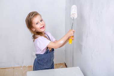 Dairede onarın. Mutlu aile anne ve kızı önlük, beyaz boya ile duvar boyası. Kız boya silindiri elinde tutan ve gülüyor. yatay çekim