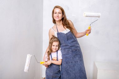 Dairede onarın. Mutlu aile anne ve küçük kızı mavi önlük, beyaz boya ile duvar boyar. Anne ve kızı boya merdaneleri tutarak ve gülümseyerek. Yatay dikey