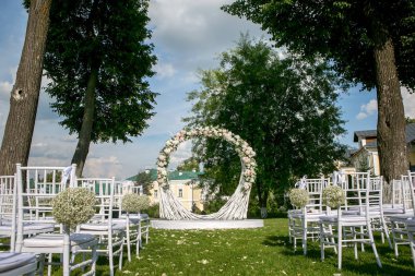 Yaz açık hava düğün töreni dekorasyon. Şube ve beyaz gül, ortanca ve yüksek ağaçlar arka plan üzerinde beyaz podyum, beyaz klasik sandalyelere gypsophila oluşan güzel beyaz kemer