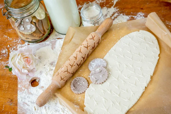 Rolling pin with a pattern on a wooden decorated table covered with baked flour. Rolled dough with a pattern and cookie of various shapes. Biscuit cooking background, top view.