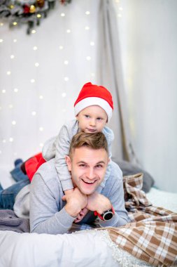 Mutlu aile, baba ve oğlu, yatak odasında sabah Noel için dekore edilmiştir. Babası üzerinde oturup Noel Baba'nın şapkalı çocuk. Yeni yıl ve Noel Tema. Tatil ruh hali.