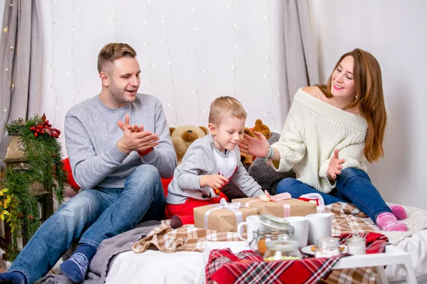 Happy family, father, mother and son, in the morning in bedroom decorated for Christmas. They open presents and have fun. New Year\'s and Christmas theme. Holiday mood.