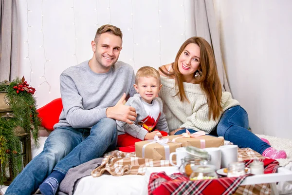 Happy family, father, mother and son, in the morning in bedroom decorated for Christmas. They open presents and have fun. New Year\'s and Christmas theme. Holiday mood.