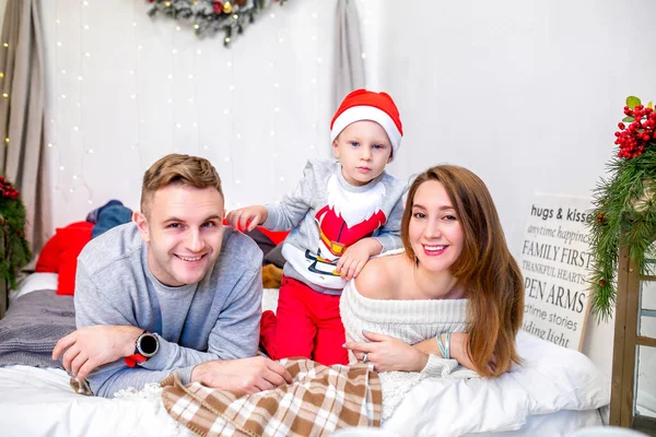 Happy family, father, mother and son, in the morning in bedroom decorated for Christmas. They open presents and have fun. New Year\'s and Christmas theme. Holiday mood.
