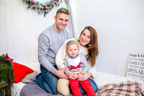 Happy family, father, mother and son, in the morning in bedroom decorated for Christmas. They hug and have fun. New Year\'s and Christmas theme. Holiday mood.