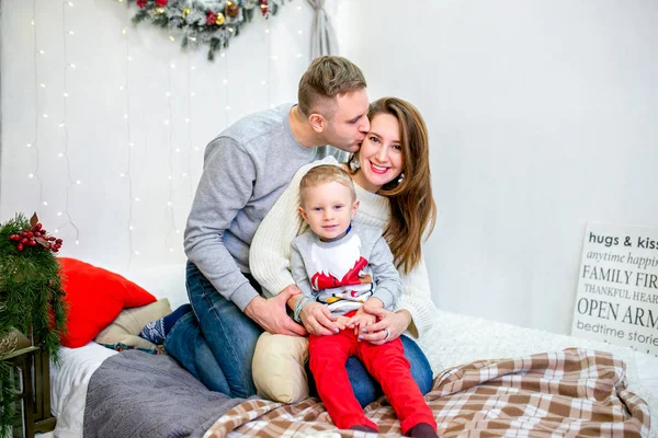 Happy family, father, mother and son, in the morning in bedroom decorated for Christmas. They hug and have fun. New Year\'s and Christmas theme. Holiday mood.