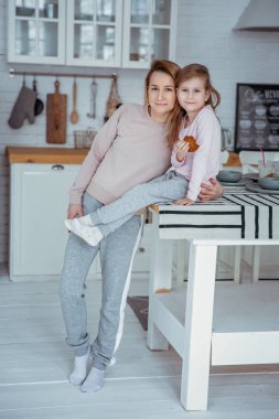 Mutlu küçük kız ve güzel genç annesi kahvaltı birlikte beyaz bir mutfak var. Anne kızı sarılmak. Anne bakım ve sevgi. Dikey fotoğraf.
