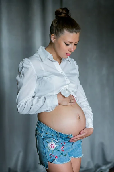 Femme enceinte heureuse touchant son ventre. Portrait de jeune mère enceinte, caressant son ventre et souriant. Concept de grossesse saine, femme enceinte brune sur fond gris — Photo
